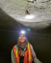 lady with a head lamp looking at a bat hanging from the ceiling 